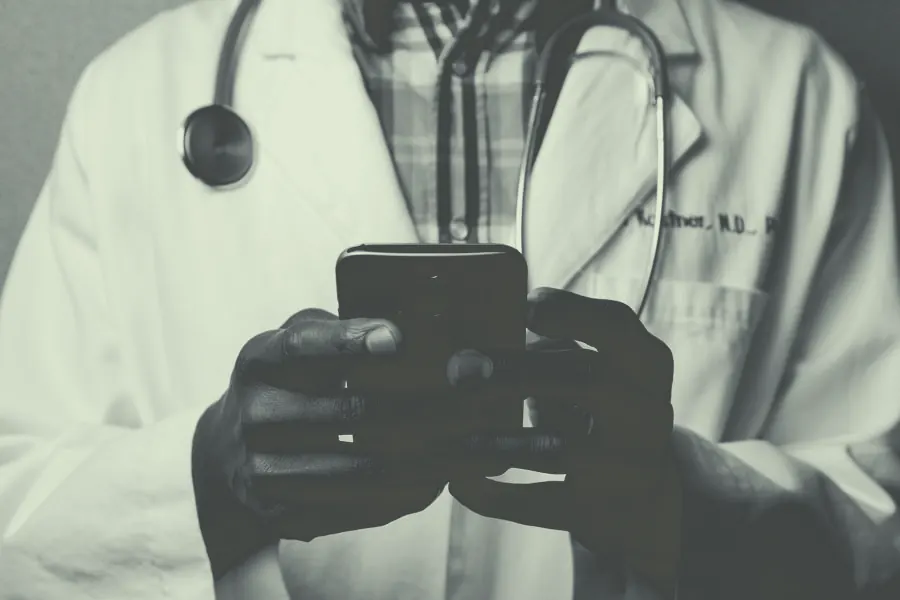 A clinician in a white coat entering notes on a handheld device.